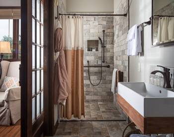 Straight on view of Square grey stone Shower with the stone continuing on the bathroom floor. Floating white sink outlined in wood